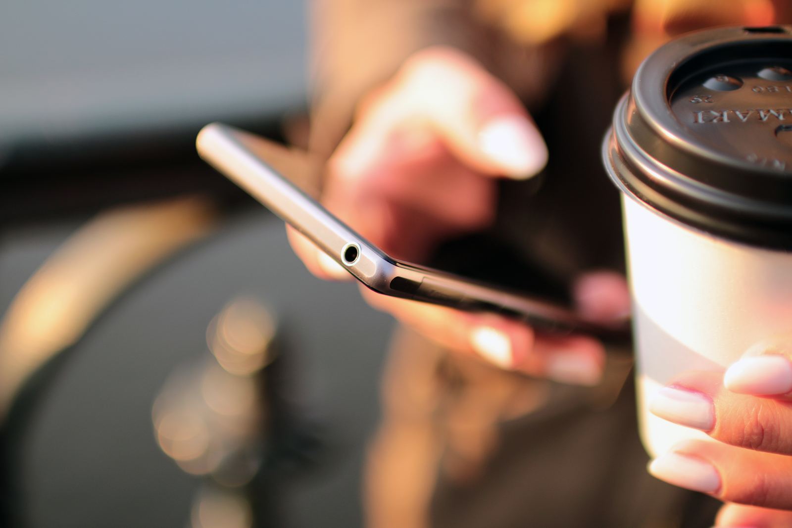 Hands holding a smartphone next to a cup of coffee